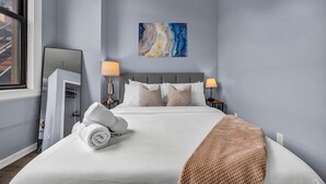 A neatly made bed with a white comforter and a beige throw blanket, a gray headboard, and a painting above it. - Cozy studio in delightful Cleveland with gym, parking and AC (Cleveland)