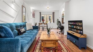 A living room with a blue sofa, a wooden coffee table, a TV stand, and a dining area with chairs and a table.