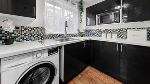 A modern kitchen with a washing machine, black cabinets, a microwave, and a tiled backsplash.