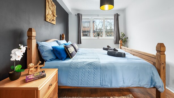 A bedroom with a bed, a nightstand, a potted plant, and a window with curtains.