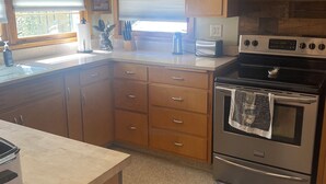 A kitchen with wooden cabinets, a stainless steel oven, and a window with blinds. - Cozy, spacious house located near historic downtown near shopping and dining. (Watertown)