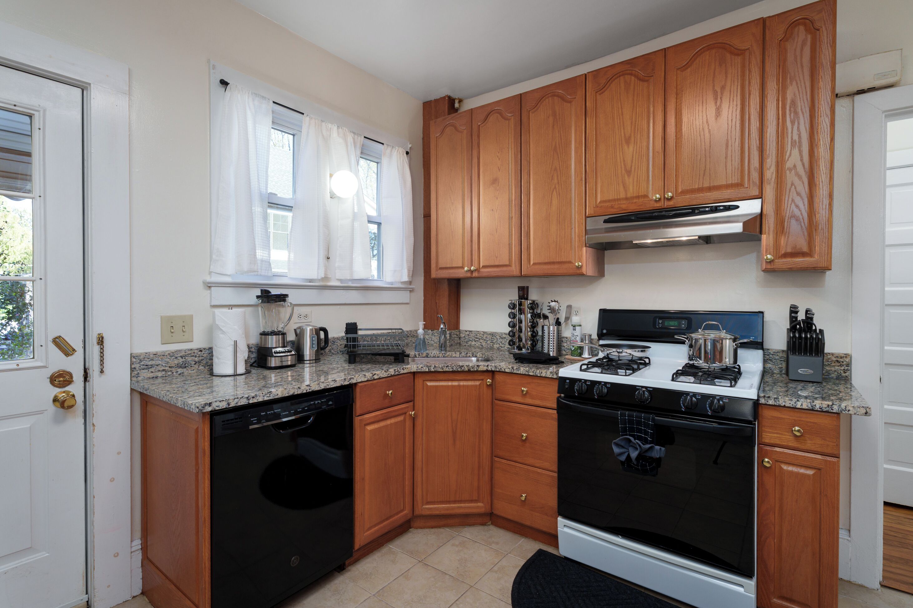 A kitchen with wooden cabinets, a stove, an oven, a dishwasher, and a window with curtains.