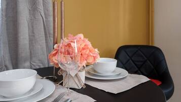 A dining table set with white plates, bowls, and cutlery, a glass with a floral arrangement, and a black upholstered chair.