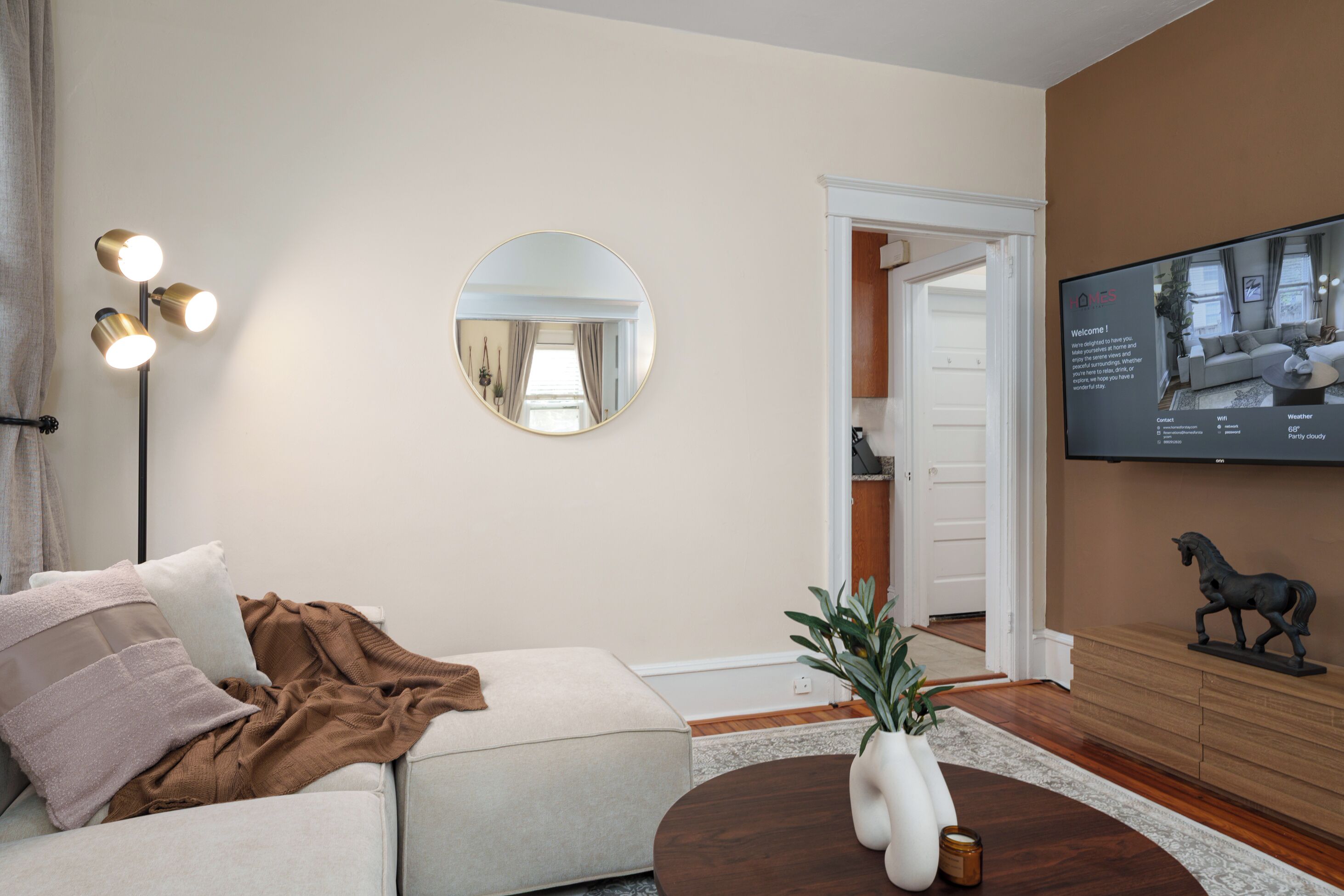 Una sala de estar moderna con un sofá, un espejo redondo, una lámpara de pie, un televisor y una estatua decorativa de un caballo.