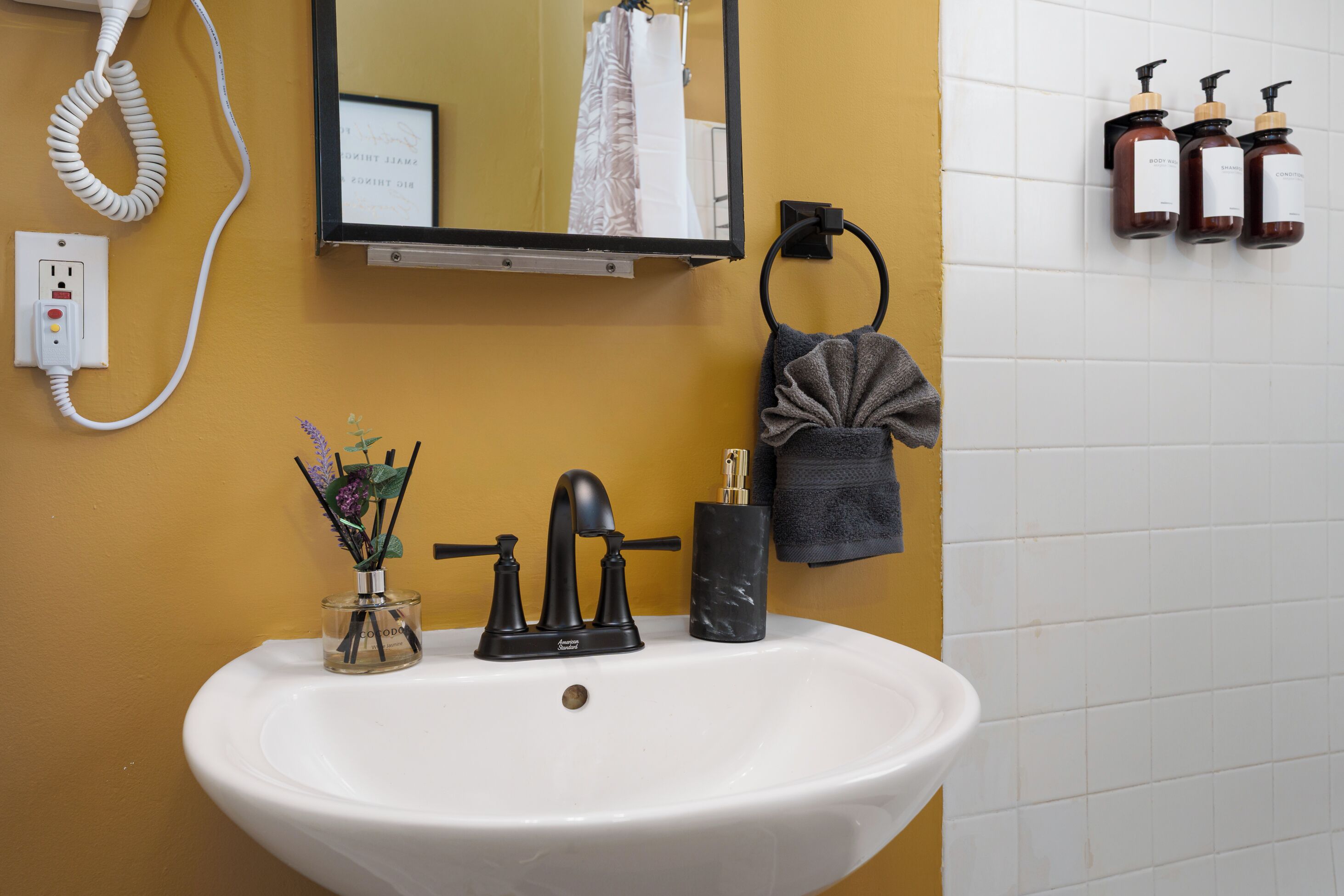 Un baño con un lavamanos blanco, un espejo, un teléfono y artículos de aseo en la pared.