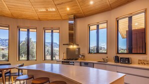 Eine moderne Küche mit einer großen Kochinsel, Barhocker und großen Fenstern mit Blick ins Freie.