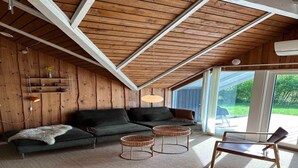 Ein gemütliches Zimmer mit Holzbalkendecke, einem dunkelgrünen Sofa, zwei Korbstühlen und einem Sessel.