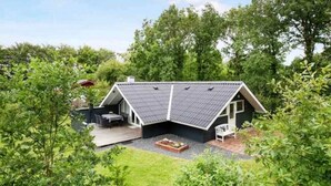 Ein modernes Haus mit einem geneigten Dach, einer Terrasse mit Gartenmöbeln und einem Gartenbereich.