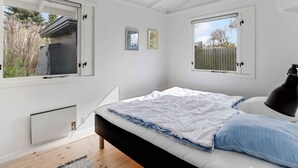 Une chambre à coucher avec un lit, deux fenêtres, un ventilateur de plafond et un radiateur.