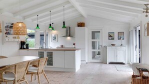Une cuisine lumineuse avec des meubles blancs, un coin repas doté de chaises en osier et des suspensions vertes.
