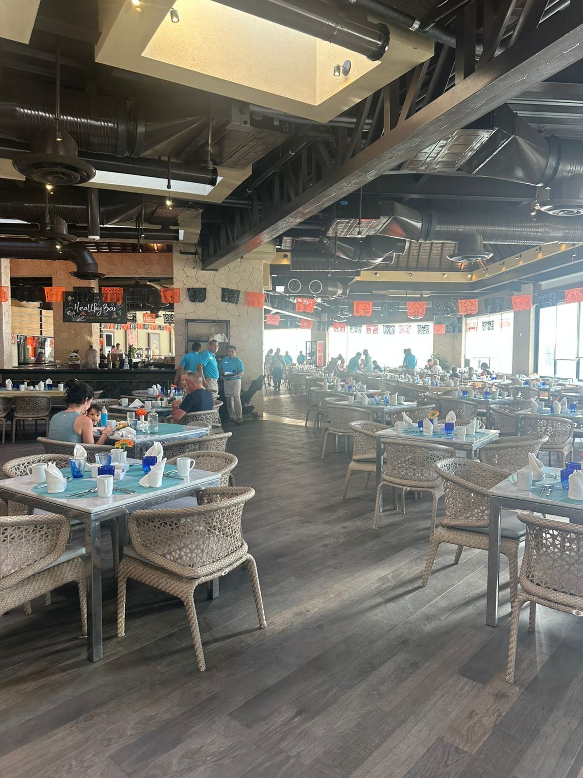 A spacious restaurant with high ceilings, exposed beams, and wicker chairs. Tables are set with blue and white tableware.