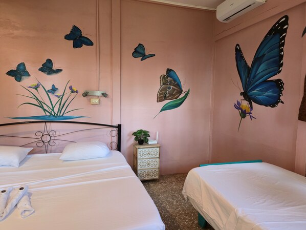 Une chambre avec deux lits, une fresque murale représentant des papillons, une petite plante sur une table de chevet et une prise de courant.