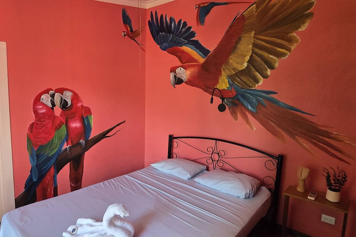 A room with a bed, a nightstand, and a wall mural of parrots.