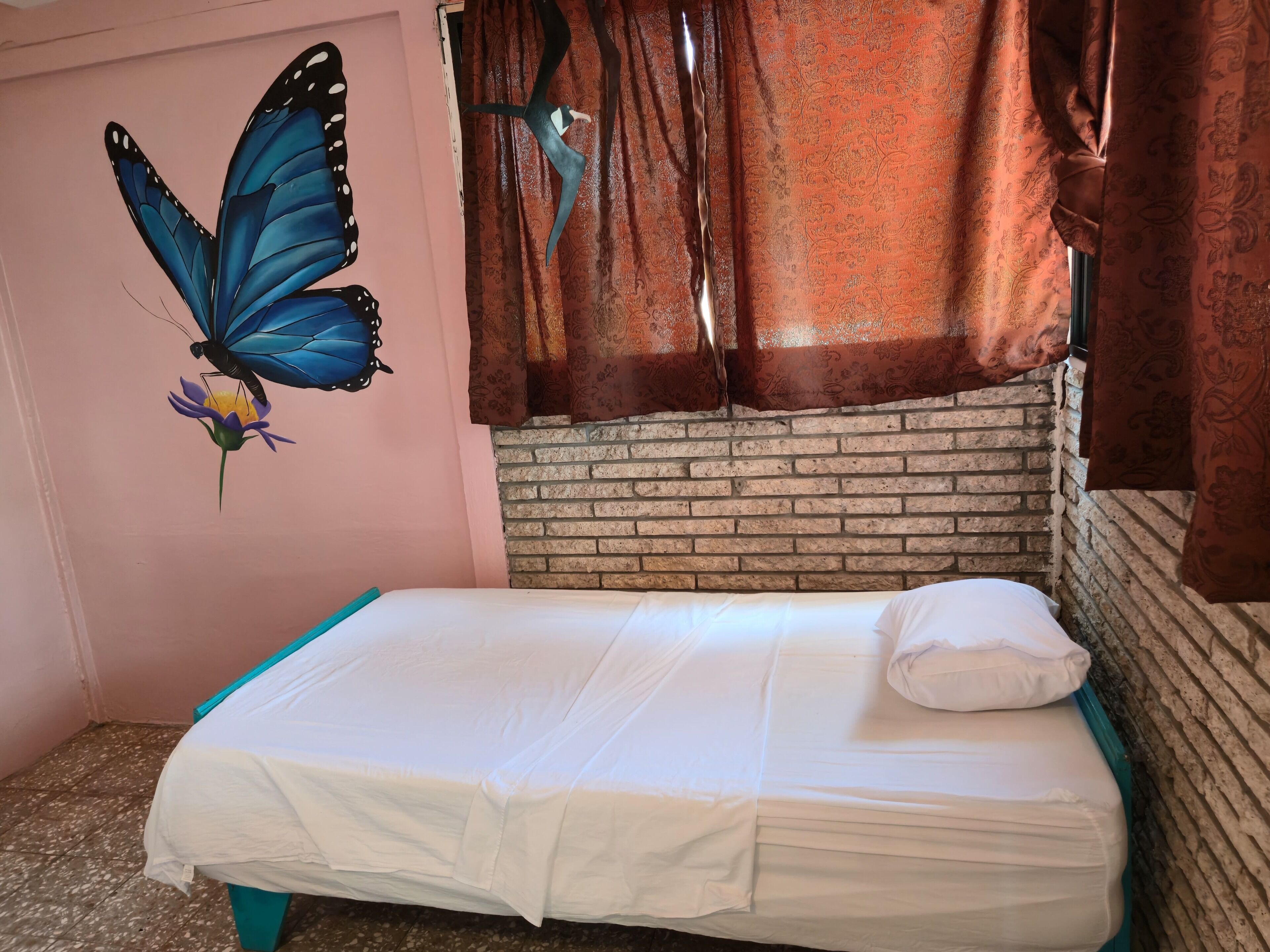 A single bed with white bedding, a brick wall, and a butterfly mural on the wall.