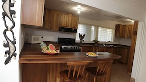 A kitchen with wooden cabinets, a microwave, a stove, and a fruit bowl on the counter. - Jane's Beach Resort (El Roble)