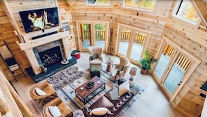 A cozy cabin interior with a fireplace, comfortable seating, and large windows.