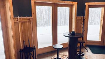 Ein Zimmer mit Holzboden, einem runden Tisch mit Hocker, einem gerahmten Kunstwerk an der Wand und großen Fenstern mit Blick auf Schnee.
