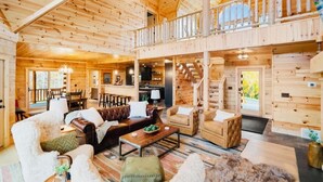 A spacious wooden cabin with a high ceiling, a cozy living area with leather sofas, a dining area, and a staircase leading to an upper level.