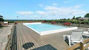 Eine Holzterrasse mit einem rechteckigen Pool, Liegestühlen und Blick auf den Ozean.