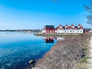 A waterfront property with a row of red and white buildings, a clear blue sky, and calm water.