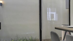 Un comedor moderno con un separador de vidrio, una mesa de madera y un estante blanco con cristalería.