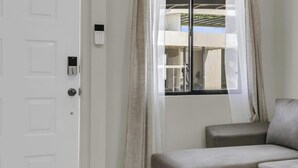 Una habitación con una puerta blanca, una ventana con cortinas y un sofá gris.