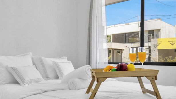 Habitación de hotel con cama, ventana que da a un edificio y bandeja con fruta y vasos de zumo de naranja.