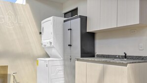 Una cocina compacta con lavadora y secadora integradas, encimera de granito y muebles de color claro.