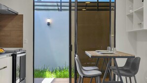 Una cocina moderna con estufa integrada, una zona de comedor con mesa y sillas, y un ventanal corredero que da a un balcón con césped.