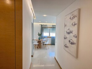 A modern interior with a dining area, a glass partition, and a wall-mounted artwork. - Apartment Flor de Amendoeira Garden | 6min from the beach, parking and pool (Albufeira)