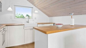 A modern kitchen with white cabinetry, a wooden countertop, and a window with a view of greenery. - 5 Star Holiday Home in Ebeltoft (Ebeltoft)