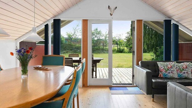 A cozy interior with a wooden dining table, teal chairs, a sofa, and a view of a grassy garden through a glass door. - 5 Star Holiday Home in Ebeltoft (Ebeltoft)