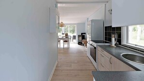 A modern kitchen with a wooden floor, white cabinets, a stainless steel sink, and a dining area with a table and chairs. - 5 Star Holiday Home in Aakirkeby (Akirkeby)