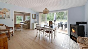 A spacious living room with a dining area, a fireplace, wicker furniture, and large windows offering a view of the outdoors. - 5 Star Holiday Home in Aakirkeby (Akirkeby)