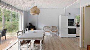 A modern kitchen with white cabinetry, a built-in oven, and a dining area with a white table and wicker chairs. - 5 Star Holiday Home in Aakirkeby (Akirkeby)