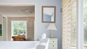 A room with a white table, a white dresser with drawers, a mirror, a lamp, and a wicker chair. - 5 Star Holiday Home in Aakirkeby (Akirkeby)