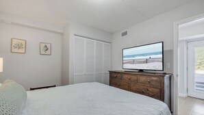 Ein Schlafzimmer mit Bett, Schminktisch, Fernseher und Blick auf den Strand durch eine Tür.