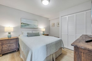 Quarto com cama, abajures, mesa de cabeceira, cómoda de madeira, guarda-roupa e um quadro na parede.
