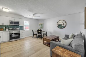 A modern kitchen with built-in appliances, a dining area with a round table and chairs, and a gray sofa in a living room.