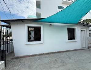 A white building with two windows and a door, a concrete ground, and a metal fence. - A block from Chipipe beach Salinas cost studio for 5  Salinas with AC (Salinas)