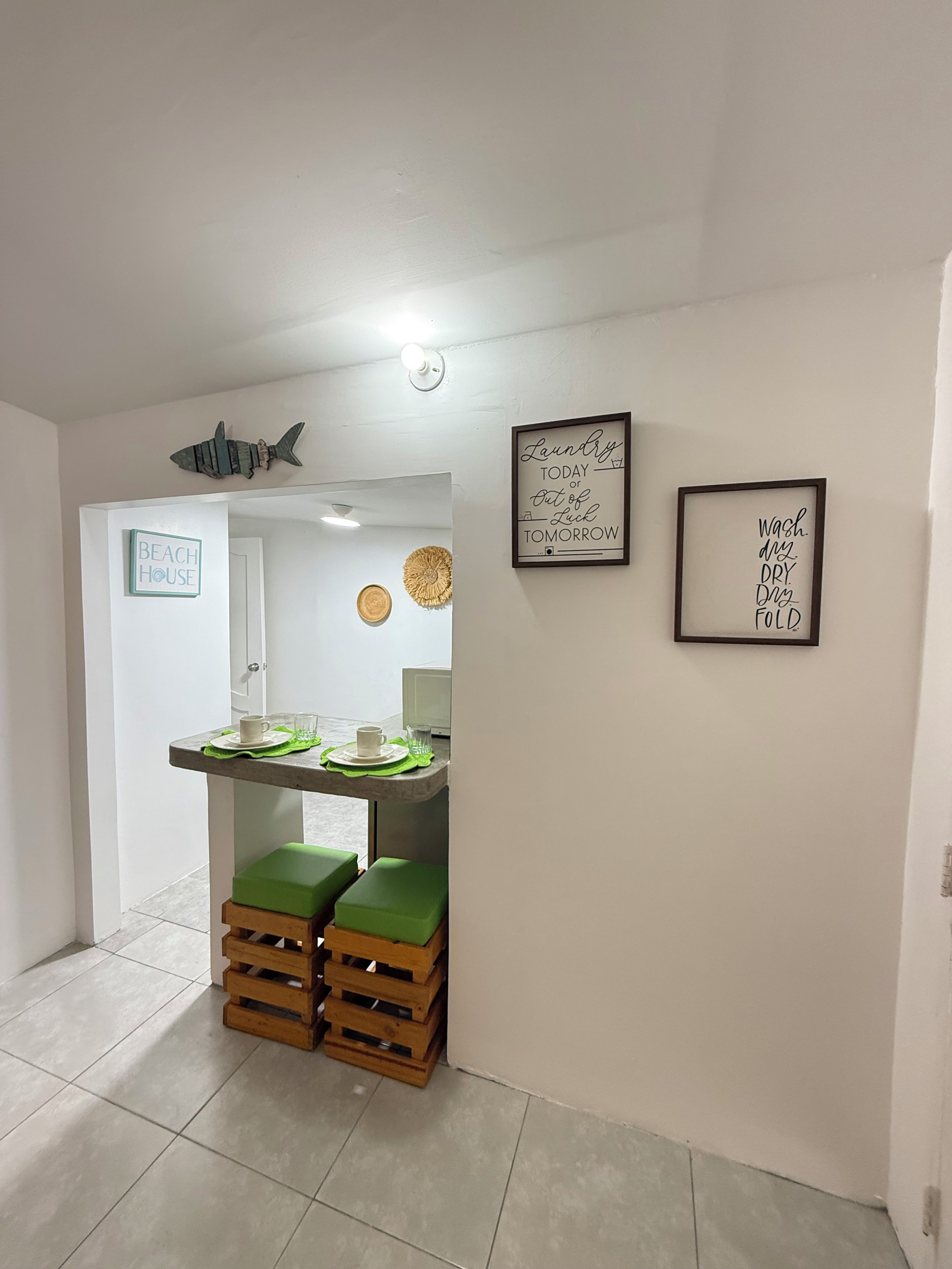A small kitchenette with a countertop, stools, and a sign that reads 'BEACH HOUSE'.