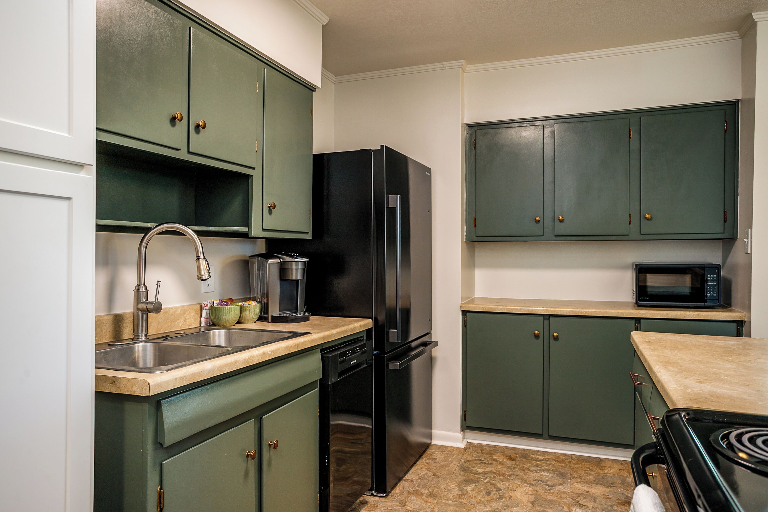 A kitchen with green cabinets, a black refrigerator, a dishwasher, a microwave, and a stove.