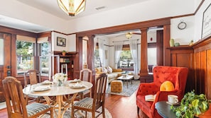 A room with a dining table set for four, a red armchair, a sofa, and a bookshelf.