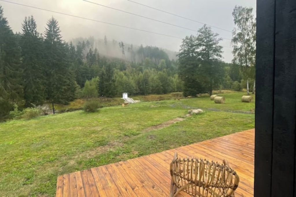 Un molo di legno con una sedia rustica, una zona erbosa con balle di fieno e un bosco sullo sfondo.