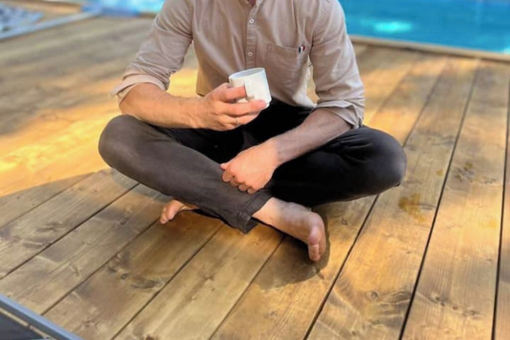 A person sitting cross-legged on a wooden deck by a pool.