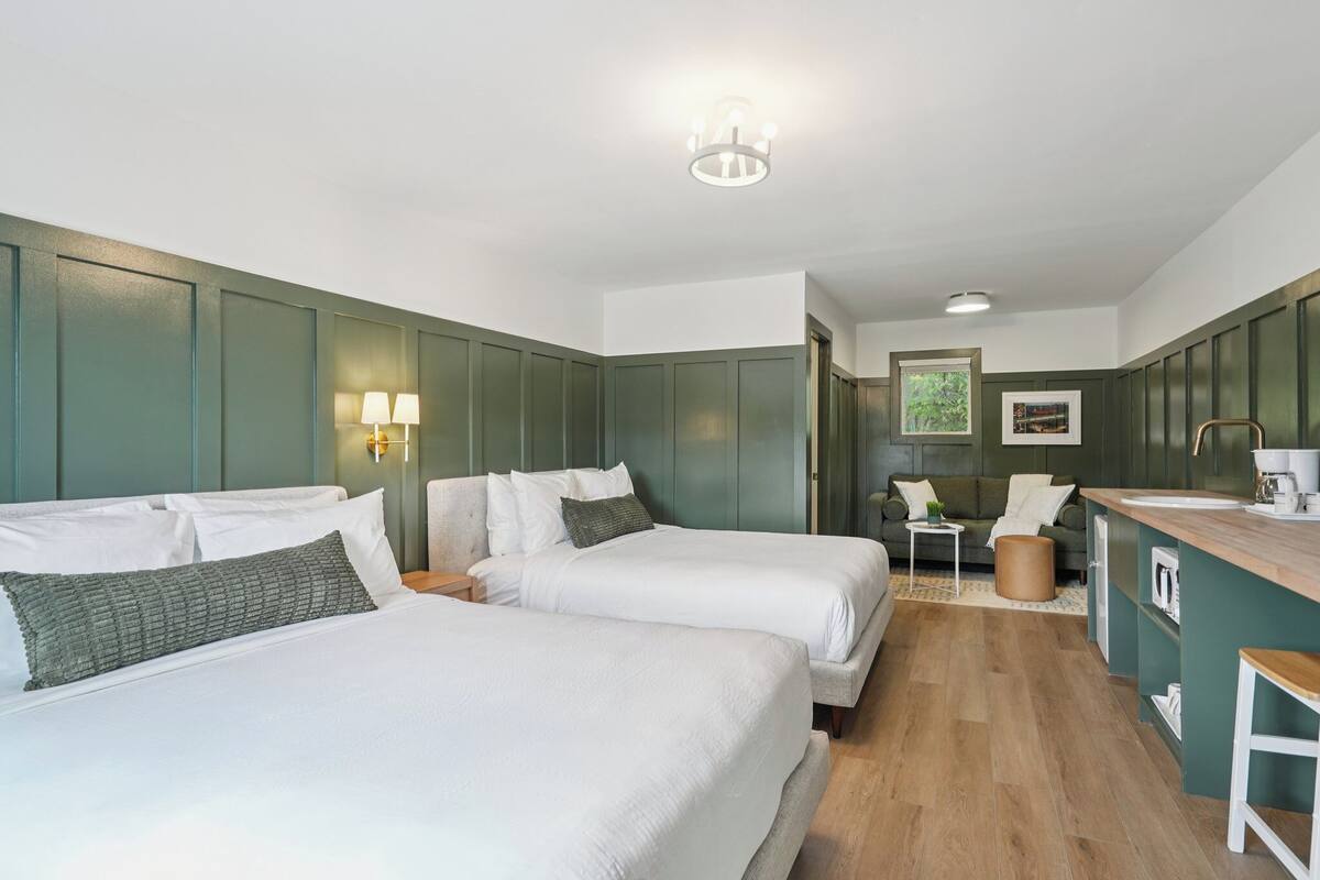 A hotel room with two beds, a kitchenette, and a dining area.