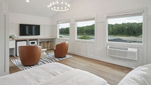 A modern room with a large window, a flat-screen TV, a kitchen area, and a cozy seating area with two brown chairs. - Lakelyn Lodge (Lakeville)