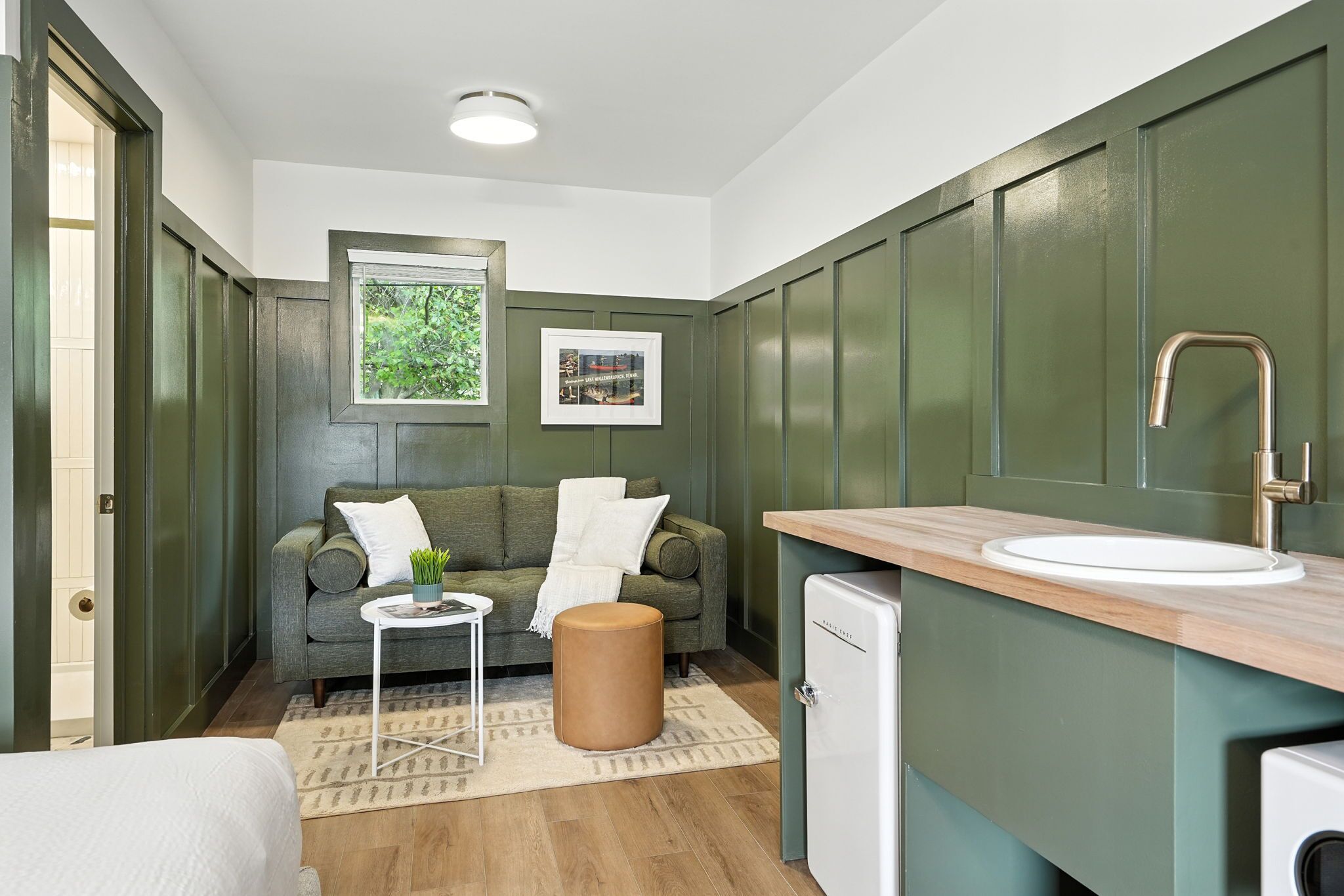 A compact room with a sofa, a small table, a stool, a sink, and a compact refrigerator.