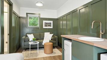 A compact room with a sofa, a small table, a stool, a sink, and a compact refrigerator.