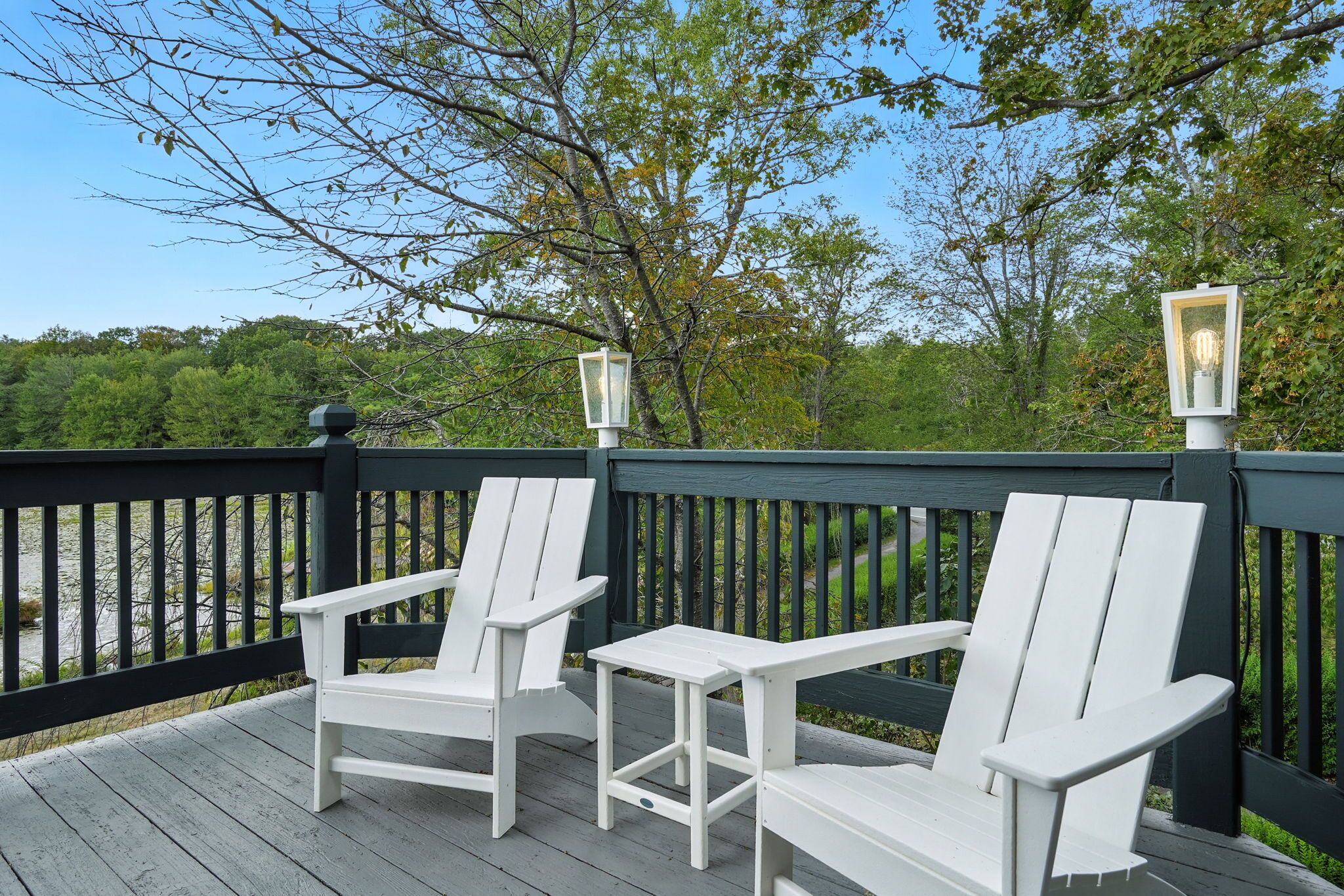 A wooden deck with two white Adirondack chairs and two lantern-style lights.